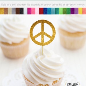 Puede incluir: Topper para cupcake con signo de paz de purpurina dorada. El topper está sobre un cupcake blanco con glaseado blanco. El cupcake está sobre una servilleta blanca. El texto "RSVP Party Decor" está en un círculo en la esquina inferior derecha de la imagen.