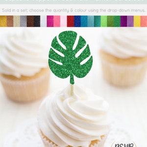 May include: Green glitter monstera leaf cupcake topper. The topper is on a white cupcake with white frosting. The cupcake is on a white doily.