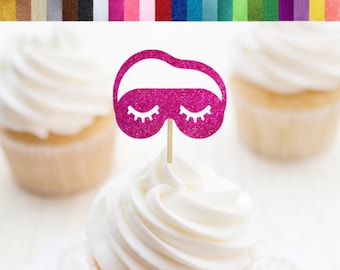 May include: Pink glitter cupcake topper shaped like a sleep mask with eyelashes. The topper is on a white cupcake with white frosting. The text "RSVP Party Decor" is visible in the bottom right corner of the image.