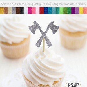 May include: Silver glitter crossed axes cupcake topper. The topper is on a white cupcake with white frosting. The cupcake is on a white doily. The text "RSVP Party Decor" is visible in the bottom left corner of the image.