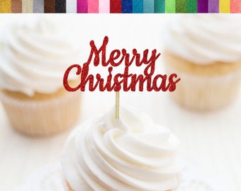 May include: A red glitter "Merry Christmas" cupcake topper on a gold stick, placed atop a cupcake with white frosting. The image features three cupcakes, with the topper centered on one. The background is blurred, highlighting the festive decoration.