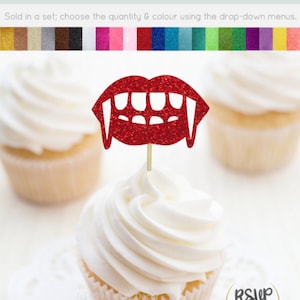 May include: Red glitter vampire teeth cupcake topper. The topper is on a white cupcake with white frosting. The cupcake is on a white doily.