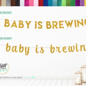 Puede incluir: Pancarta de brillo dorado con el texto "A BABY IS BREWING" en letras de bloque y "a baby is brewing" en letras de escritura. La pancarta está colgada en una pared blanca. El texto "RSVP PARTY DECOR" está en un círculo con fondo verde y texto blanco. El texto "MORE FONTS AVAILABLE!" está debajo de la pancarta.