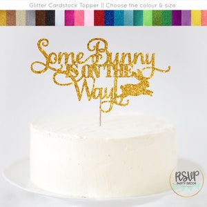 May include: Gold glitter cardstock cake topper with the text "Some Bunny is on the Way" and a bunny silhouette.