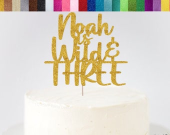 Puede incluir: Topper para pastel de cartulina con purpurina dorada que dice "Noah is Wild & Three".