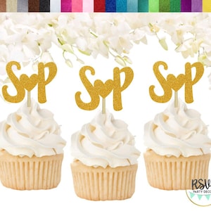 May include: Three gold glitter cupcake toppers with the letters "S" and "P" with a heart in between. The toppers are on top of cupcakes with white frosting.