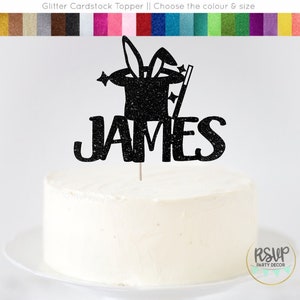 May include: Black glitter cardstock cake topper featuring a magician's hat, rabbit ears, and a wand. The name "JAMES" is written below the hat.