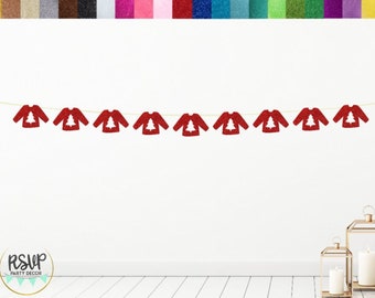 Puede incluir: Una guirnalda de suéteres rojos brillantes con un diseño de árbol de Navidad blanco, colgada en una pared blanca. La guirnalda está completamente montada. La parte superior de la imagen muestra una paleta de colores brillantes.