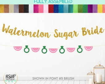May include: Watermelon Sugar Bride banner with gold glitter letters and pink and green watermelon and ring cutouts. The banner is fully assembled and ready to hang.