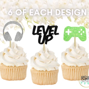Puede incluir: Seis adornos para cupcakes con diseños de purpurina. Los adornos representan unos auriculares, las palabras "Level Up" y un mando de videojuego verde.
