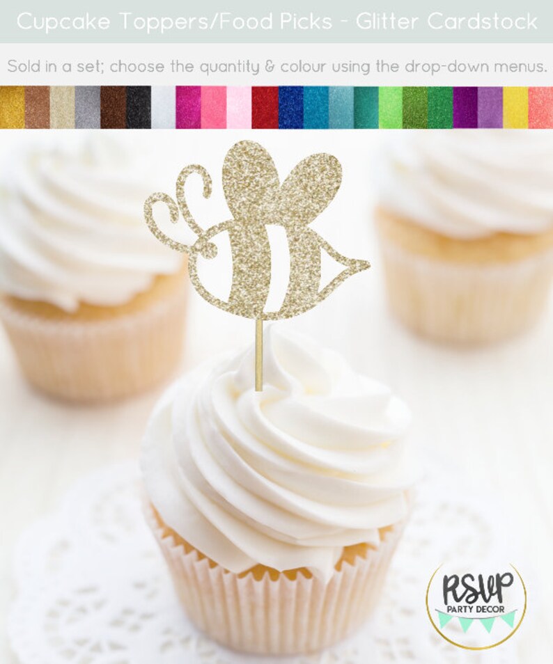 May include: Gold glitter bee cupcake topper. The bee has a striped body and is on a wooden stick. The topper is on a white cupcake with white frosting.