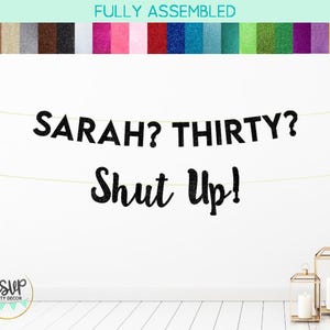 May include: Black glitter banner with the text "SARAH? THIRTY? SHUT UP!" hanging on a white wall.