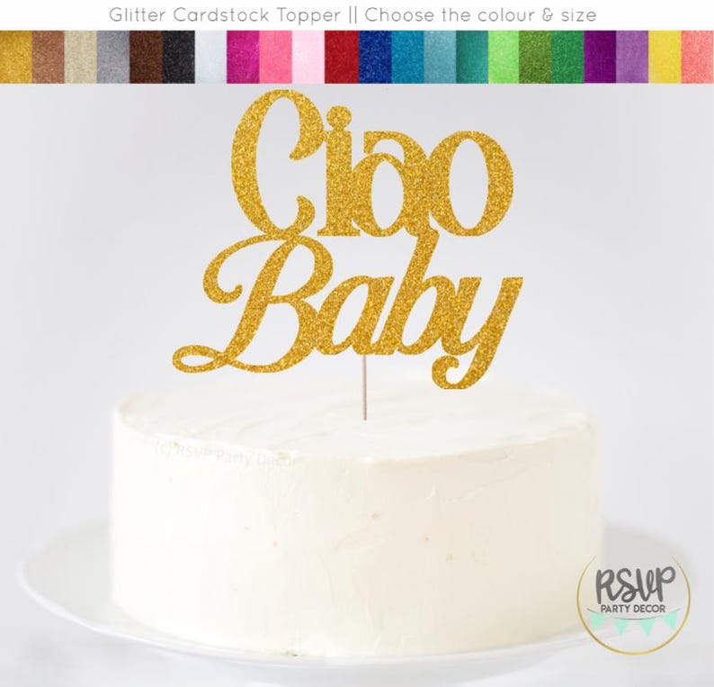 K&ouml;nnte beinhalten: Eine wei&szlig; glasierte Torte mit einem goldglitzernden "Ciao Baby" Tortenaufsatz. Der Aufsatz ist an einem d&uuml;nnen, silbernen Stab befestigt. Die Torte steht auf einem wei&szlig;en Teller. Oben im Bild ist eine Farbkarte aus Glitzerkarton zu sehen.