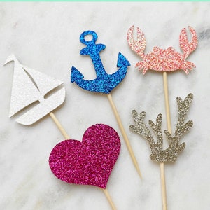 May include: Set of six glitter cupcake toppers featuring a sailboat, anchor, crab, heart, and reindeer antlers. The toppers are made in sets of six per design.  "Mix & Match" and "Visit our shop for hundreds of other designs" are written at the top of the image.