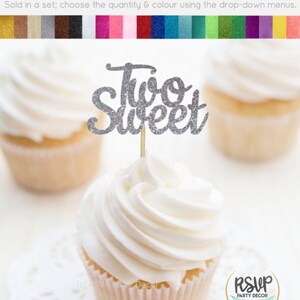 May include: Silver glitter cupcake topper with the words "Two Sweet" on a white cupcake.
