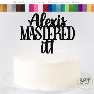 May include: Black glitter cardstock cake topper with the text "Alexis Mastered it!"