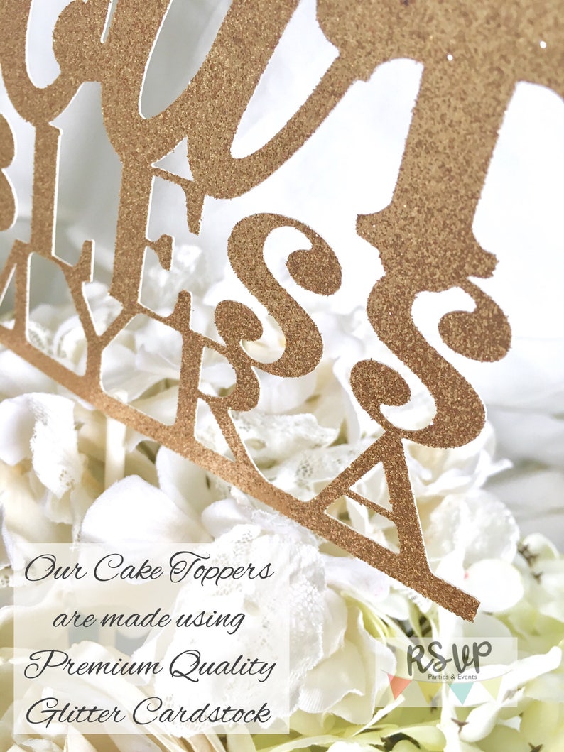 May include: Gold glitter cake topper with the words "Our Bless Myra" on it. The topper is sitting on a white cake with white flowers. The text "Our Cake Toppers are made using Premium Quality Glitter Cardstock" is visible below the cake topper. The text "RSUP Parties & Events" is visible in the bottom right corner of the image.