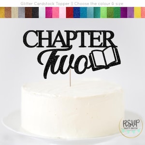 May include: A black glitter cake topper with the words "CHAPTER Two" and an open book illustration. The topper is placed on a white iced cake. A colour chart is visible at the top of the image.
