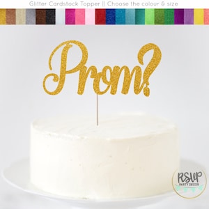 May include: Gold glitter cake topper that says "Prom?" in a cursive font. The topper is on a white cake.