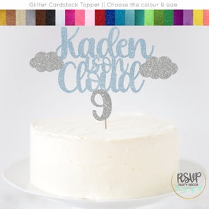 May include: A blue glitter cardstock cake topper with the name "Kaden" and the words "is on cloud 9" with silver glitter clouds and a silver glitter number 9.