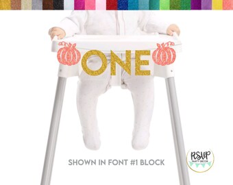 May include: A high chair with a banner reading "ONE" in gold glitter letters. The banner features coral glitter pumpkins. The text "SHOWN IN FONT #1 BLOCK" is below the high chair. A party decor logo is in the bottom right.