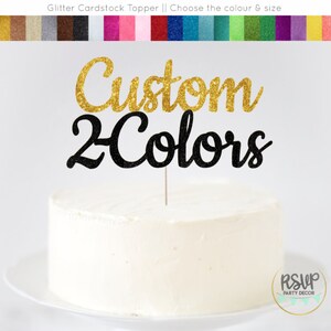 May include: Gold glitter "Custom" and black glitter "2 Colors" cake topper. The topper is on a white cake.