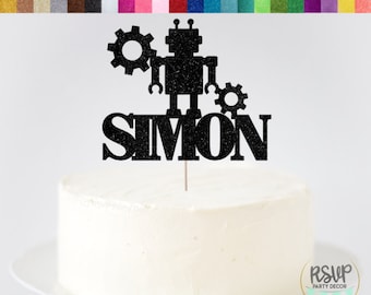 May include: Black glitter cardstock cake topper featuring a robot with gears and the name "SIMON".