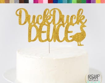 May include: A gold glitter cardstock cake topper with the words "Duck Duck Deuce" and a duck silhouette. The topper is on a white iced cake. A colour chart of glitter cardstock options is at the top of the image.