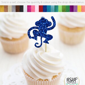 K&ouml;nnte beinhalten: Blauer Glitzer-Affen-Cupcake-Topper. Der Affe sitzt mit einem erhobenen Arm. Der Topper befindet sich auf einem wei&szlig;en Cupcake mit wei&szlig;em Frosting.