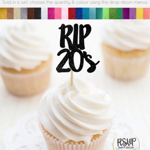 May include: Black glitter cupcake topper with the text "RIP 20s". The topper is on a cupcake with white frosting. The cupcake is on a white doily.