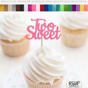 May include: Pink glitter cupcake topper with the text "Two Sweet" on a stick. The topper is on top of a cupcake with white frosting.