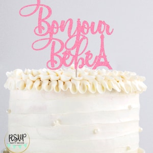 May include: Pink glitter cake topper with the text "Bonjour Bebe" and a small Eiffel Tower design.