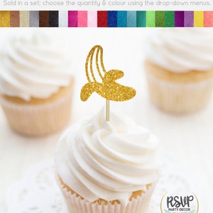 May include: Gold glitter cupcake topper shaped like a banana. The topper is on a white cupcake with white frosting. The cupcake is on a white doily. The text "RSVP Party Decor" is visible in the lower right corner of the image.