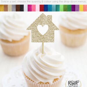 May include: Gold glitter cupcake topper shaped like a house with a heart cut out. The topper is on a white cupcake with white frosting. The text "RSVP Party Decor" is on a sticker on the cupcake.