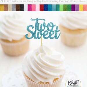 May include: Two blue glitter cupcake toppers with the text "Two Sweet" on a white cupcake with white frosting.