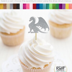May include: Silver glitter dragon cupcake topper with wings. The topper is on a cupcake with white frosting. The cupcake is on a white doily. The image also shows a color chart of glitter cardstock.