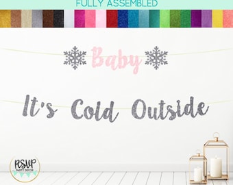 May include: A glittery banner with the words "Baby" and "It's Cold Outside" in silver and pink. The banner is decorated with snowflake shapes. The words "FULLY ASSEMBLED" are at the top. The banner is for a baby shower.