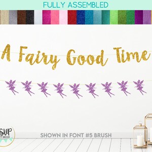 Puede incluir: Una pancarta dorada con purpurina que dice "A Fairy Good Time" con siluetas de hadas de purpurina morada colgando de ella. La pancarta está completamente ensamblada y lista para colgar.