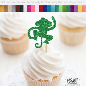 K&ouml;nnte beinhalten: Gr&uuml;ner Glitzer-Affen-Cupcake-Topper. Der Affe sitzt mit erhobenen Armen und dem Schwanz um sein Bein gewickelt. Der Topper befindet sich auf einem wei&szlig;en Cupcake mit wei&szlig;em Frosting.