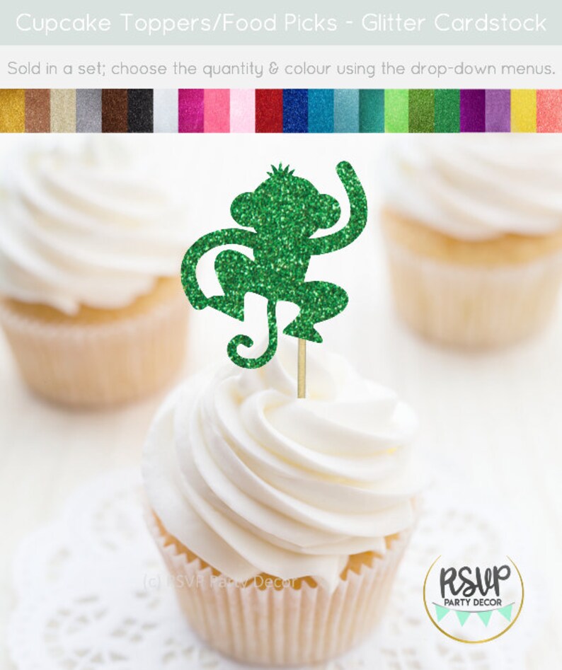 K&ouml;nnte beinhalten: Gr&uuml;ner Glitzer-Affen-Cupcake-Topper. Der Affe sitzt mit erhobenen Armen und dem Schwanz um sein Bein gewickelt. Der Topper befindet sich auf einem wei&szlig;en Cupcake mit wei&szlig;em Frosting.