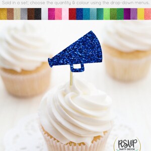 May include: A cupcake topped with a blue glitter megaphone-shaped food pick. The cupcake has white frosting and sits on a white doily. The image includes other cupcakes and a color palette.