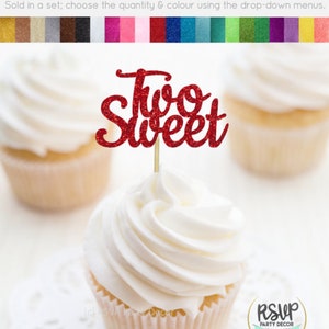 May include: Red glitter cupcake topper with the words "Two Sweet" on it. The topper is on a cupcake with white frosting.