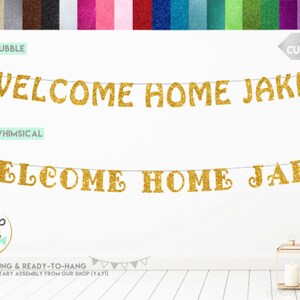 Pode incluir: Faixa de purpurina dourada com o texto "WELCOME HOME JAKE" em duas fontes diferentes. A faixa &eacute; pr&eacute;-enfiada e pronta para pendurar.