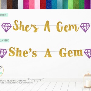 May include: Gold glitter banner with the text "She's A Gem" and purple diamond shapes. The banner is pre-strung and ready to hang.