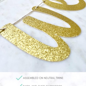 May include: Gold glitter banner with the word "We" on it. The banner is assembled on neutral twine and made of thick, anti-shed cardstock. The font and color can be customized.