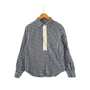 May include: A long-sleeve shirt featuring a navy blue and white gingham check pattern. The shirt has a pointed collar, a single chest pocket, and a white button-down placket that extends halfway down the front. It is displayed on a wooden hanger.