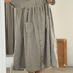 Pu&ograve; includere: Un abito midi a quadri vichy verde e bianco con chiusura a bottoni sul davanti e due tasche a toppa. L'abito ha una vestibilit&agrave; rilassata e una gonna leggermente svasata.