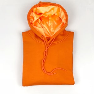May include: Orange hoodie with a satin lining. The hoodie has a drawstring and is folded in half.