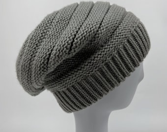 May include: A gray knitted beanie with a slouchy fit. The beanie is made of a soft, comfortable material and has a ribbed texture.