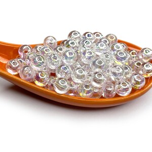 Peut inclure: Gros plan d'une petite cuill&egrave;re en c&eacute;ramique orange remplie de perles de verre transparentes et iris&eacute;es.